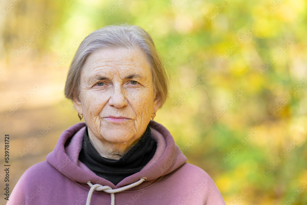 Happy gray-haired woman in a purple tracksuit with a hood and a white drawstring. Looks at the camera with a smile. Copy space Happy gray-haired woman in a purple tracksuit with a hood and a white drawstring. Looks at the camera with a smile. Copy space