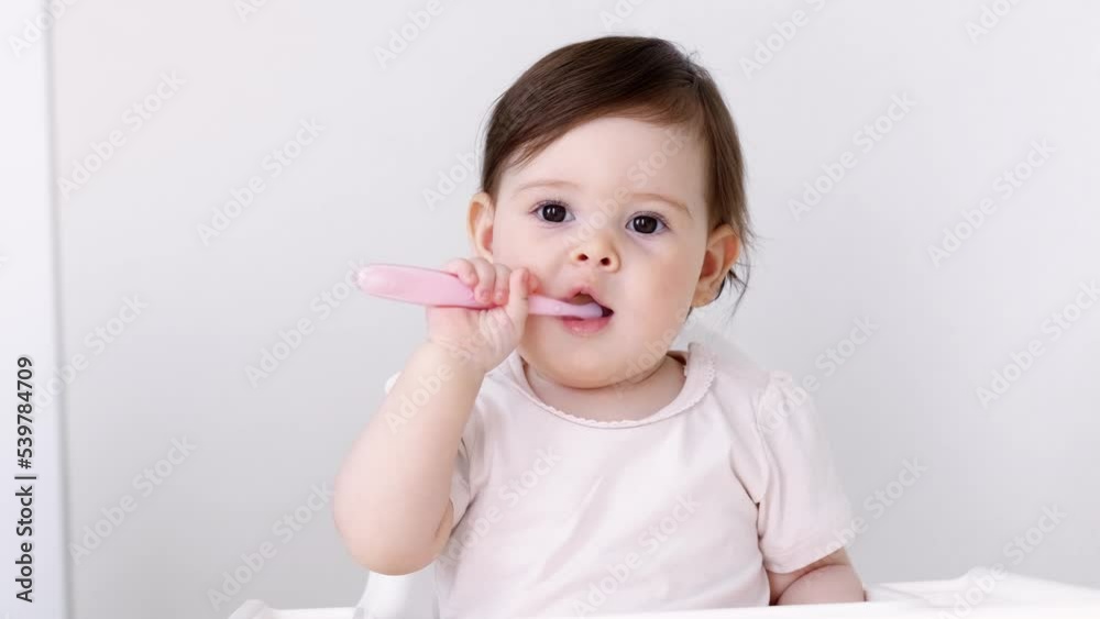 Portrait cute baby girl on kitchen sitting on high chair, smiling child happy to eat first solid food putting spoon in mouth Portrait cute baby girl on kitchen sitting on high chair, smiling child happy to eat first solid food putting spoon in mouth