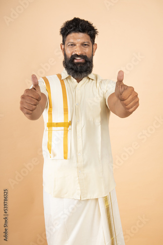 Happy Confident South indian man do thumbs up with both hands isolated on beige background. photo