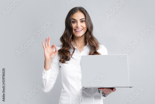 Young beautiful female teacher or happy student isolated on gray studio background. Portrait of college student with laptop. Woman working on laptop, freelance.