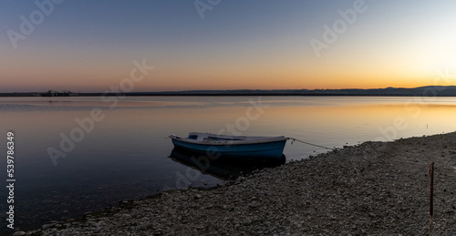 sunset over Lake Budeasa in central Romania with a wooden rowboat tied up on the rocky beach