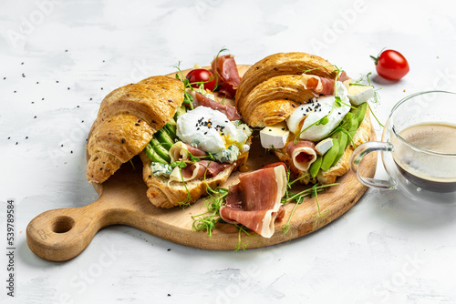 Croissant with prosciutto, poached egg, jamon, blue, cheese, avocado, microgin and cherry tomatoes. Mediterranean appetizer. Breakfast concept photo