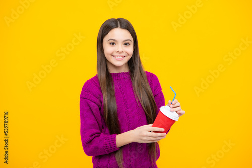 Child with coffee or tea cup isolated on yellow studio background. Teenage girl with take away beverage.