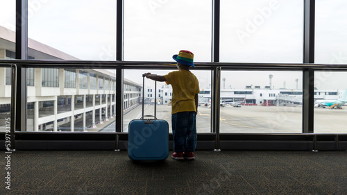 Child with suitcase at airport terminal waiting for departure looking out the window. Child and suitcase at the airport, indoors and waiting for going to travel.
