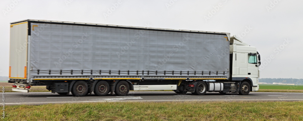 Heavy gray awning semi truck drive on highway road . Side view . Transportation logistics Heavy gray awning semi truck drive on highway road . Side view . Transportation logistics