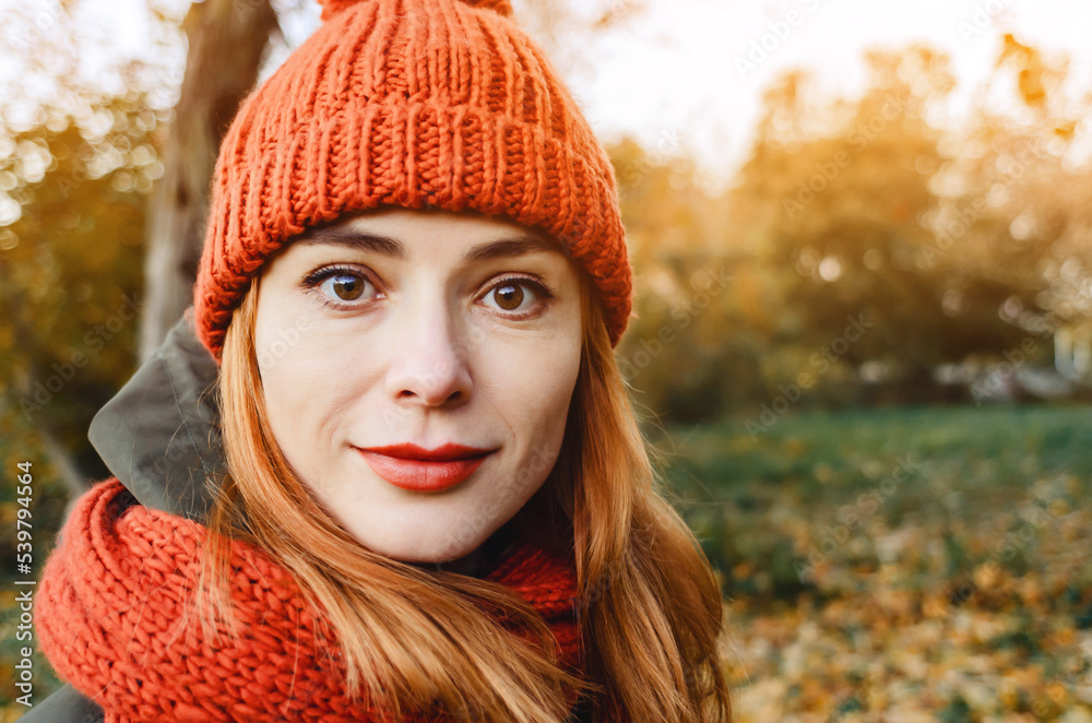 Autumn portrait of a stylish woman in an orange warm knitted hat and an orange scarf. Romantic look of big eyes. Looks into the camera close-up. Autumn portrait of a stylish woman in an orange warm knitted hat and an orange scarf. Romantic look of big eyes. Looks into the camera close-up.