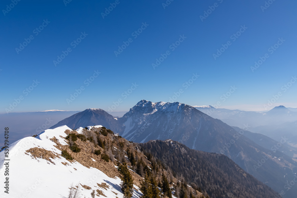 Panoramic view from summit of Freiberg on snow capped mountain peak Hochobir in Karawanks, Julian Alps, Carinthia, Austria. Winter wonderland on sunny day in Austrian Alps, Europe. Ski tour hiking