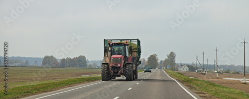 Obraz na płótnie Big red wheeled tractor with heavy trailer on countryside highway road on field w salonie