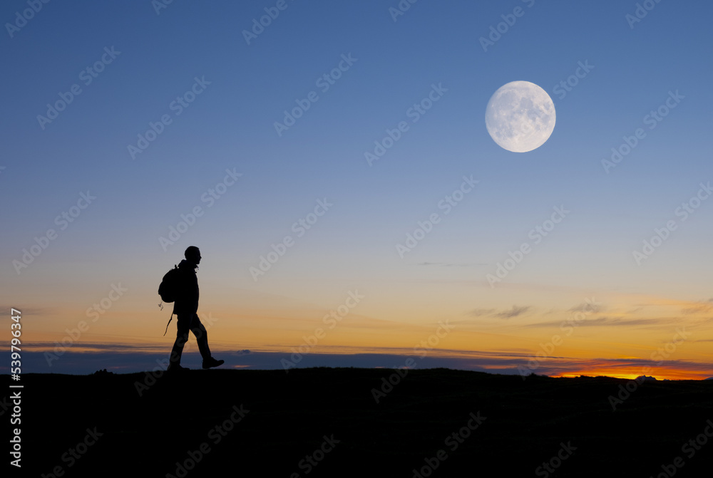 Hiker walking under the full moon at dusk.