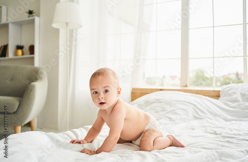 Cute baby in a diaper on the bed in the bedroom.