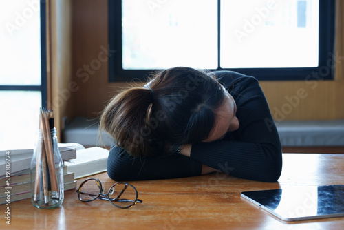 A portrait of a teenage Asian woman sleeping on a desk in the library due to fatigue from studying