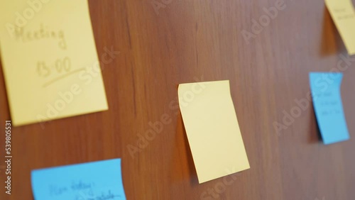 The girl sticks a blank sticker for notes on a wooden wall. A woman glues a blank note.