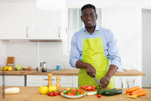 African american man in an apron cooks cuts vegetables for making soup in kitchen