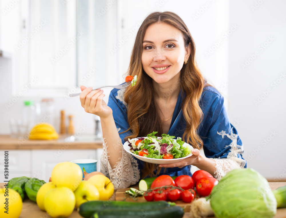 Portrait of woman standing in home kitchen and tasting vegetable salad Portrait of woman standing in home kitchen and tasting vegetable salad