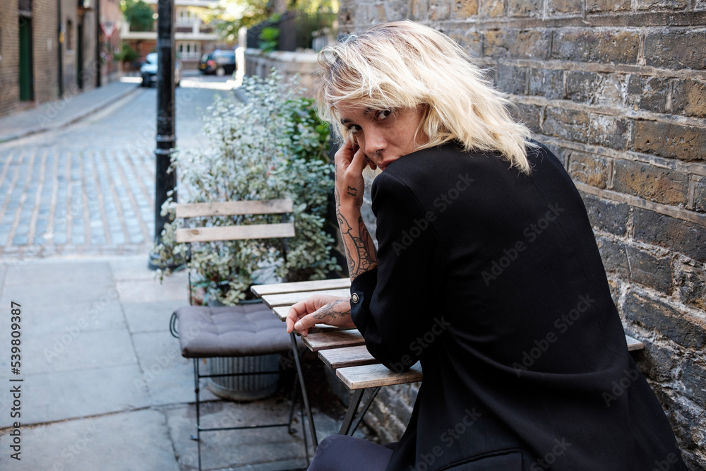 Young alternative woman is sitting on a terrace table and looking back. Young alternative woman is sitting on a terrace table and looking back.