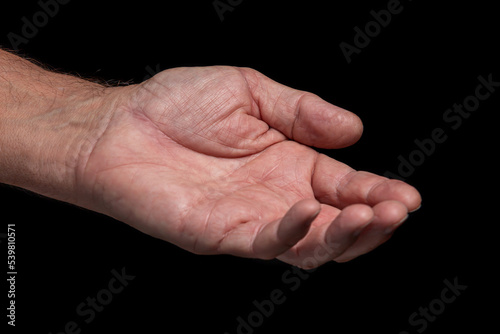 Closeup, wrinkled left hand of an elderly man asks for help on a black background.  