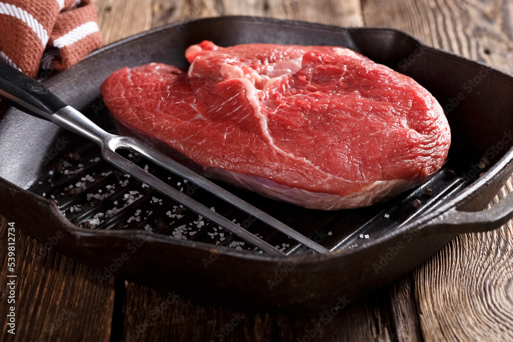 Raw piece of meat for grilling with vegetables in a cast iron pan, close-up, eating out, studio photo