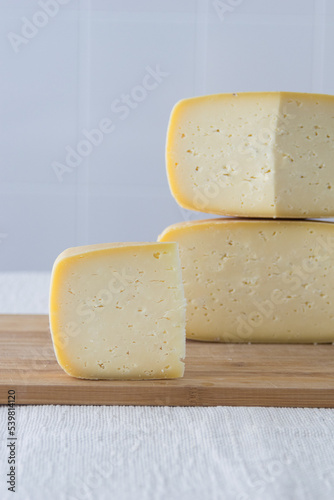 Cutted round partmesan or pecorino cheese head on wooden board on light background. Fresh dairy product, healthy organic food, selective focus, copyspace. Delicious appetizer.