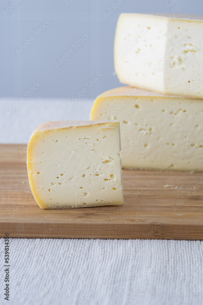 Cutted round partmesan or pecorino cheese head on wooden board on light background. Fresh dairy product, healthy organic food, selective focus, copyspace. Delicious appetizer.