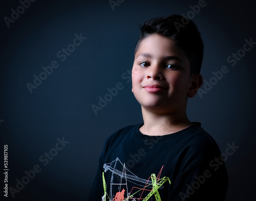 cute boy posing and smiling in a photography studio with a black T-shirt and black background 
