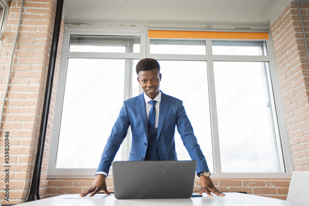Fototapeta premium portrait of stylish african man in suit at table with laptop 
