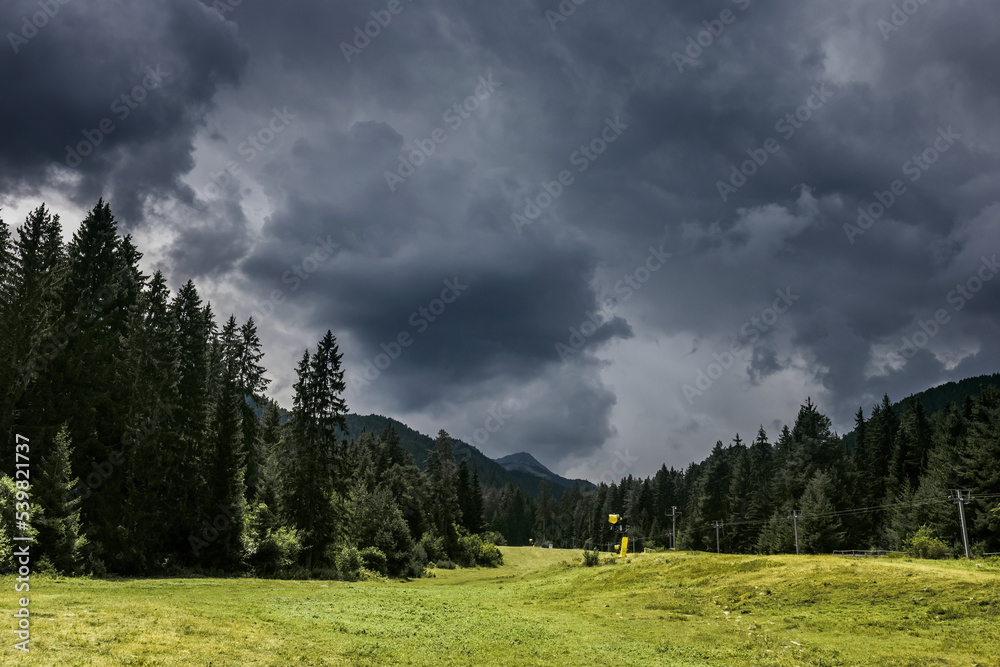 Stormy summer day in Chalin valog. Dark dramatic clouds over the Todorka peak, pine forest and ski slope in Pirin mountains near Bansko, Bulgaria. Stormy summer day in Chalin valog. Dark dramatic clouds over the Todorka peak, pine forest and ski slope in Pirin mountains near Bansko, Bulgaria.