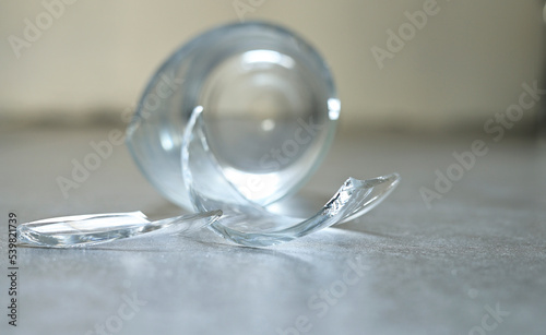Empty drinking glass falling on the gray tile floor and cracked to small shattered and sharp. Closeup broken beverage glass crash, accident in home