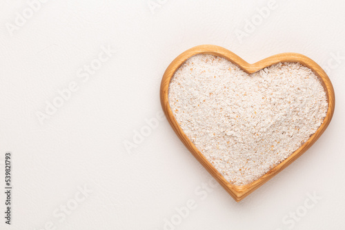 Wheat flour in a wooden heart shape bowl on a pastel background.