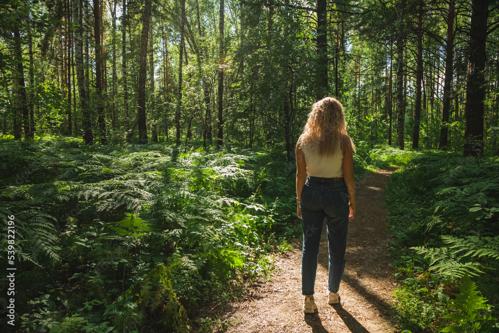 The young woman walks through a dark forest on a sunny day The young woman walks through a dark forest on a sunny day