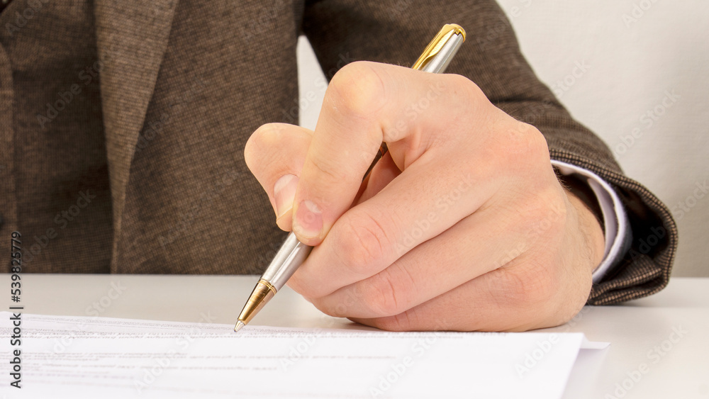 close shot of a human hand writing something on the paper on the foreground, business concept close shot of a human hand writing something on the paper on the foreground, business concept