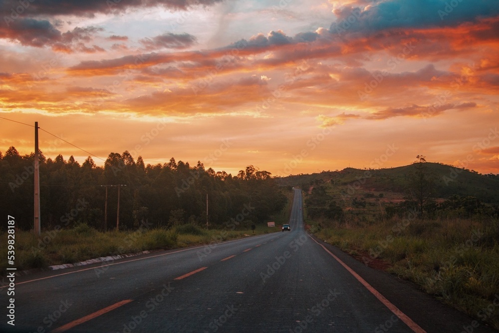 Black asphalt road and yellow dividing lines at sunset.
Car with headlights on