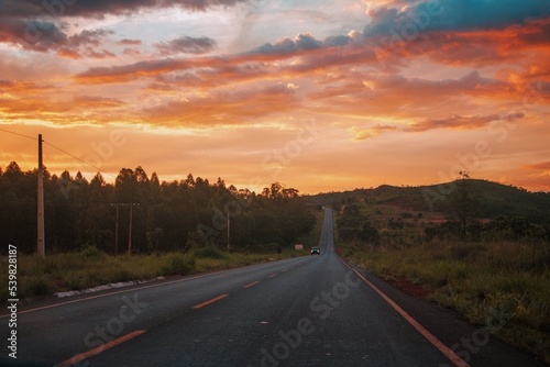 Black asphalt road and yellow dividing lines at sunset. Car with headlights on