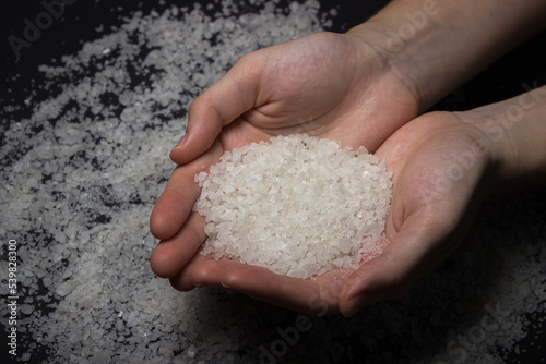 Hands holding coarse rock salt on a black background. Large salt crystals