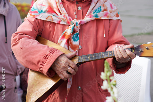 An elderly woman plays an old vintage balalaika on a city street. Street musician.
