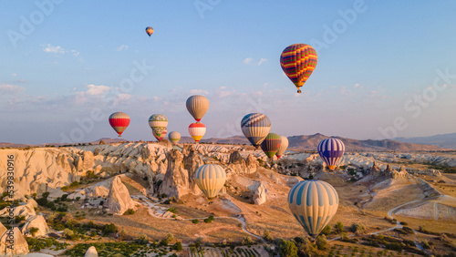 Cappadocia hot air balloons ride above rocky landscape of natural formations at sunrise in central Turkey.