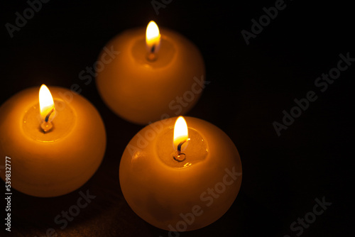 Burning bright golden candles on black background. Festive or mourning candles.
