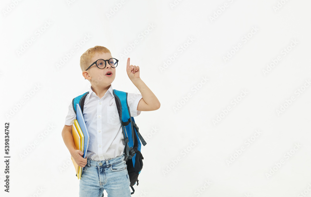 Back to school. Funny little boy from elementary school with a book, a backpack and glasses on a white background. Laughs merrily. Preparation for school. Concept of early development Back to school. Funny little boy from elementary school with a book, a backpack and glasses on a white background. Laughs merrily. Preparation for school. Concept of early development