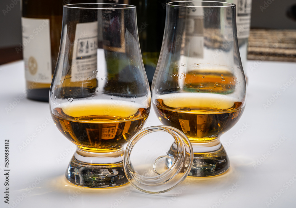 Tasting of whiskey, tulip-shaped tasting glasses with dram of Scotch single malt or blended whisky on white table Tasting of whiskey, tulip-shaped tasting glasses with dram of Scotch single malt or blended whisky on white table