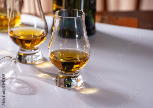 Tasting of whiskey, tulip-shaped tasting glasses with dram of Scotch single malt or blended whisky on white table