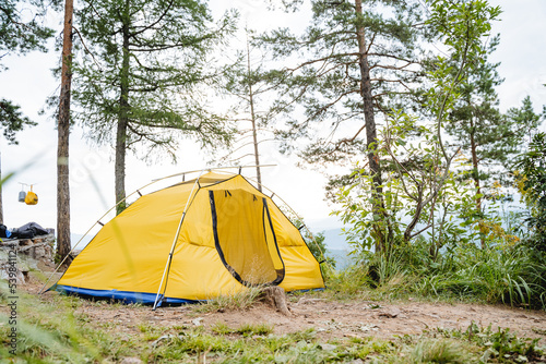 A yellow tent stands in the forest high in the mountains, tourist camping, a summer day in nature, a vacation in the forest, an open entrance.