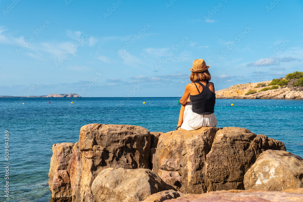 Vacation concept, A young woman in a hat by the sea in Ibiza at Salada y Saladeta beach. Balearic