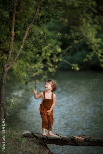 children walk on the bridge across the river fishing with a stick play in summer in overalls