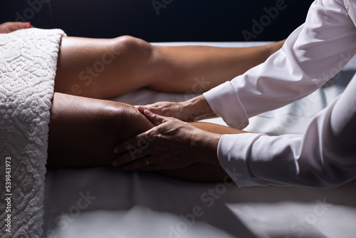 Massoterapeuta fazendo massagem no joelho de paciente deitada em maca.