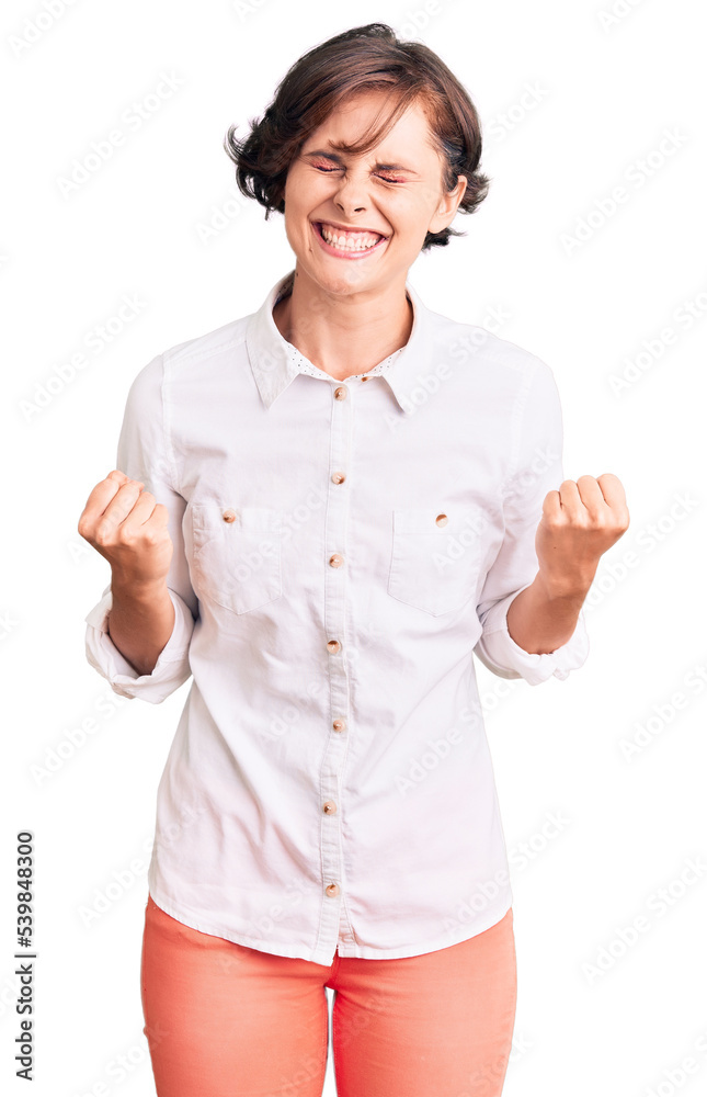 Beautiful young woman with short hair wearing elegant white shirt very happy and excited doing winner gesture with arms raised, smiling and screaming for success. celebration concept. Beautiful young woman with short hair wearing elegant white shirt very happy and excited doing winner gesture with arms raised, smiling and screaming for success. celebration concept.
