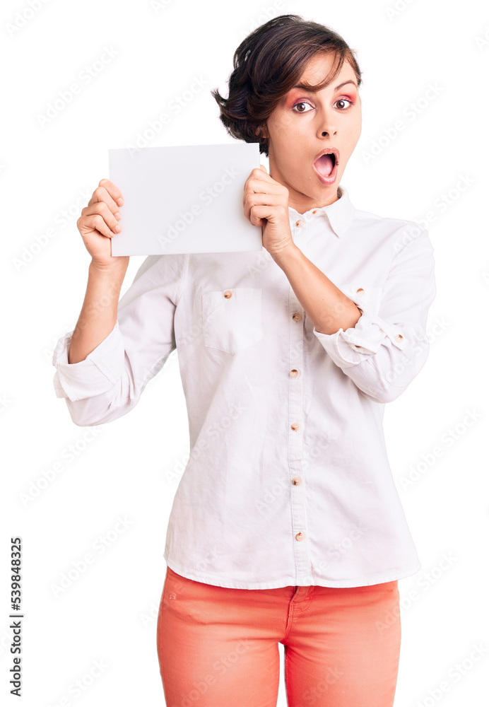 Beautiful young woman with short hair holding blank empty banner scared and amazed with open mouth for surprise, disbelief face Beautiful young woman with short hair holding blank empty banner scared and amazed with open mouth for surprise, disbelief face