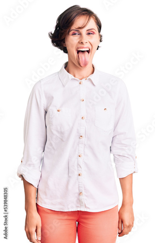 Beautiful young woman with short hair wearing elegant white shirt sticking tongue out happy with funny expression. emotion concept.