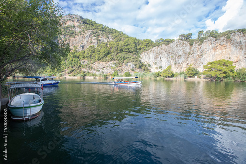 The rock-cut temple tombs of the ancient city of Kaunos in Dalyan, Muğla, Turkey. Beautiful view of Dalyan river with reed beds, excursion boats and carved tombs in the background.