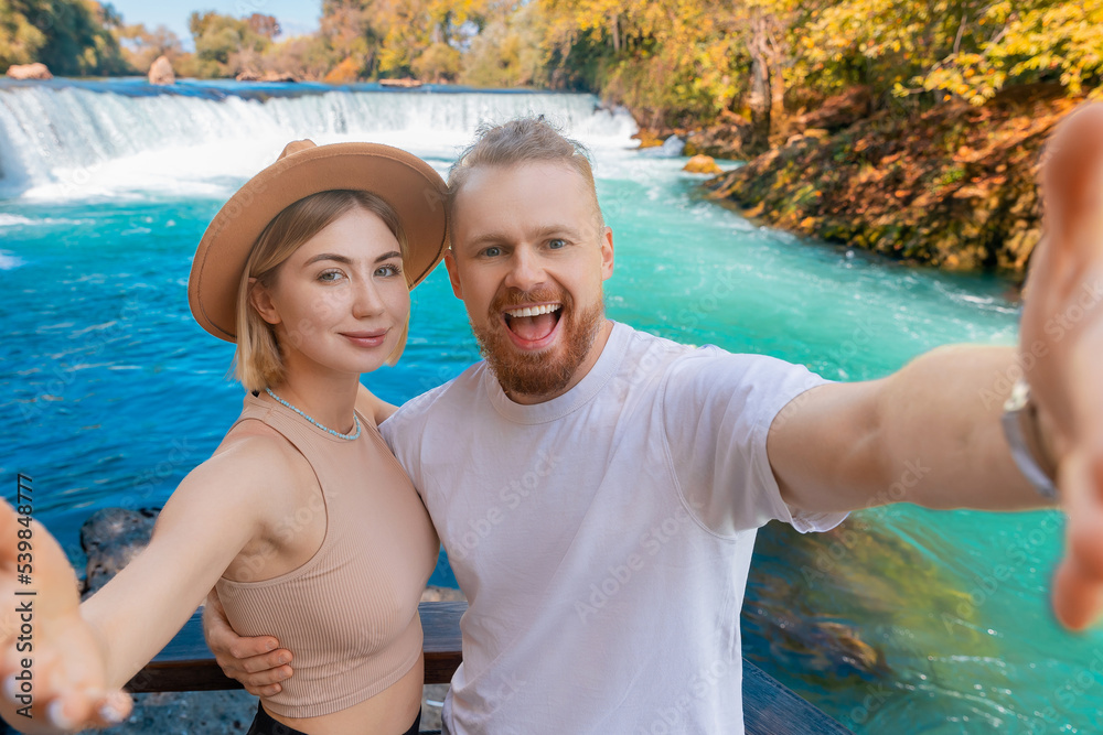 Fototapeta premium Happy tourist woman and man make selfie photo on smartphone background waterfall summer Manavgat Antalya. Concept travel trip Turkey