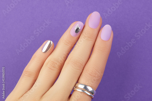 Close up womans hand with matte lavender nail design on purple background. Manicure, pedicure beauty salon