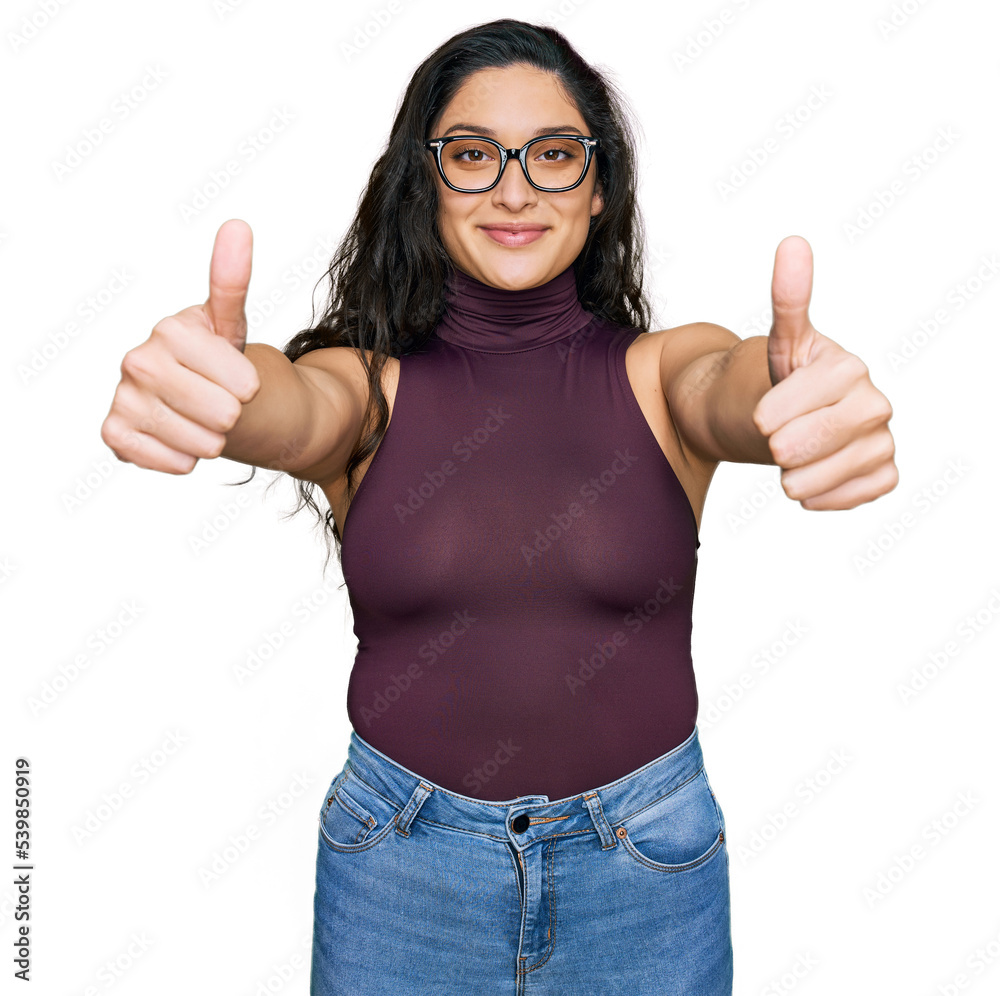 Brunette young woman wearing casual clothes and glasses approving doing positive gesture with hand, thumbs up smiling and happy for success. winner gesture. Brunette young woman wearing casual clothes and glasses approving doing positive gesture with hand, thumbs up smiling and happy for success. winner gesture.